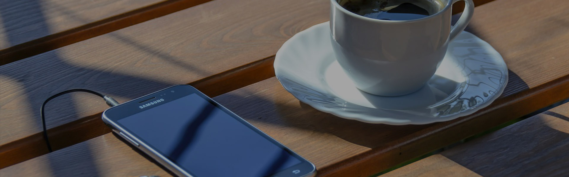 Fotografía de una taza de café junto a un teléfono celular con audífonos, sobre una superficie de madera.