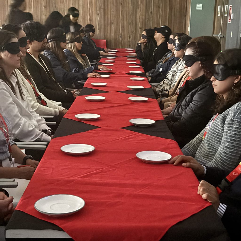 Fotografía del público en una función de Más Historia, con los ojos vendados frente a una mesa.
